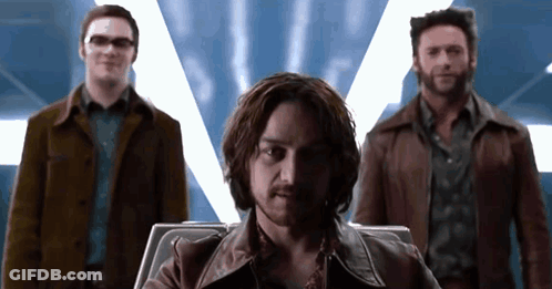 Man With Beard Sitting In Chair With Two Men Standing Behind GIF