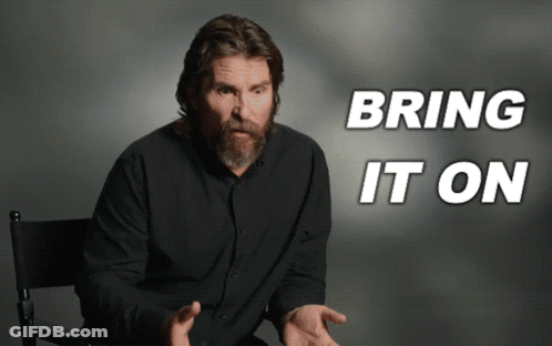 Man With Beard Sitting In Front Of Bring It On Sign GIF