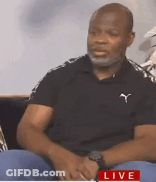 Man With Beard Sitting On Couch In Black Polo Shirt GIF