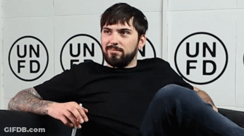 Man With Beard Sitting On Couch In Front Of Un Fd Wall GIF