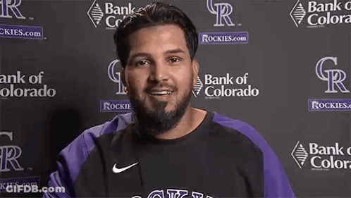 Man With Beard Smiling In Front Of Bank Of Colorado Logos GIF