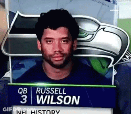 Man With Beard Standing In Front Of Russell Wilson Sign GIF