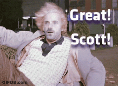 Man With Blonde Hair And Mustache Sitting In Front Of Great Scott Sign GIF
