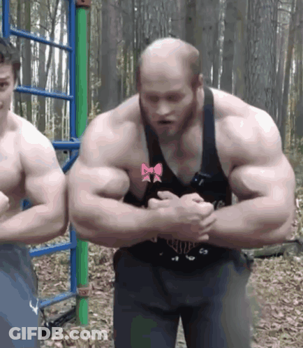 Man With Bow On Chest Flexing Muscles Next To Another Man GIF