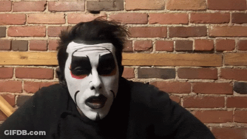 Man With Clown Face Sitting By Brick Wall GIF