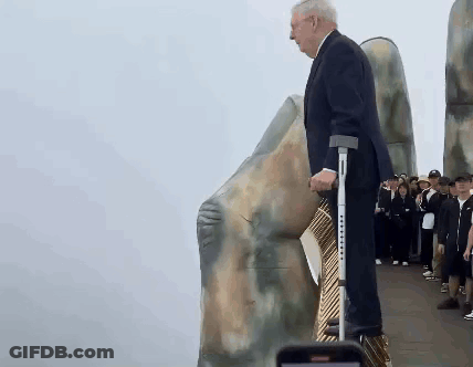 Man With Crutches Standing In Front Of Large Rock GIF