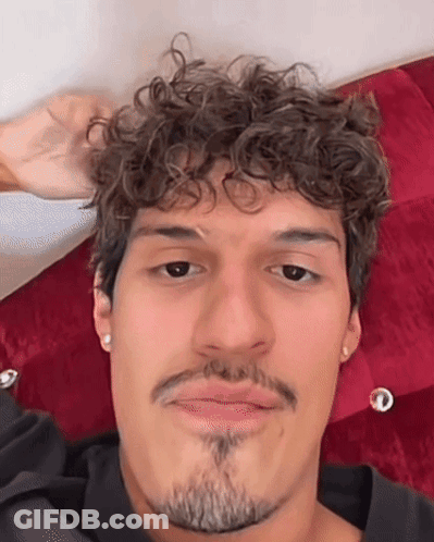 Man With Curly Hair And Beard Laying On Bed Making Funny Face GIF
