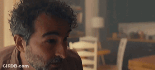 Man With Curly Hair And Beard Sitting At Table GIF