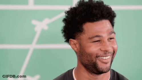 Man With Curly Hair And Beard Smiling In Front Of Green Board GIF