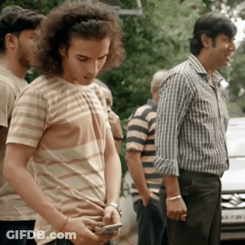 Man With Curly Hair Checking Phone In Line GIF