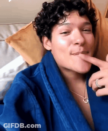 Man With Curly Hair In Blue Robe And Necklace Licking Lips GIF