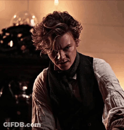 Man With Curly Hair In Vest And Scarf Looking At Camera GIF