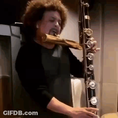 Man With Curly Hair Playing Bassoon In Dark Room GIF