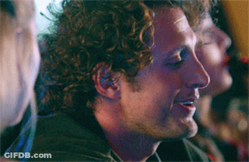 Man With Curly Hair Smiling In Dark Room GIF