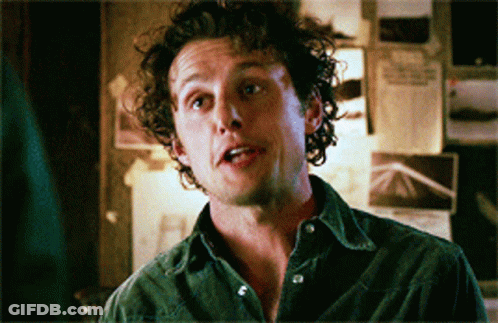 Man With Curly Hair Standing In Front Of Wall With Papers GIF