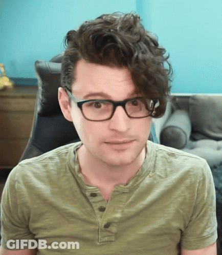 Man With Curly Hair Wearing Glasses And Green Shirt Looks At Camera GIF
