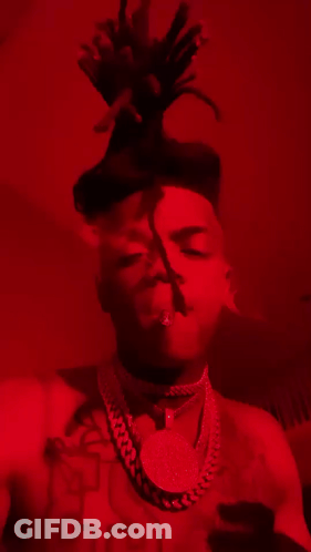 Man With Dreadlocks And Necklace Smoking In Red Room GIF