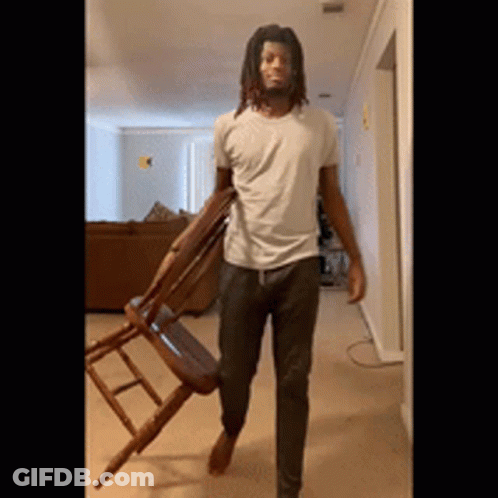 Man With Dreadlocks Carrying Wooden Chair GIF