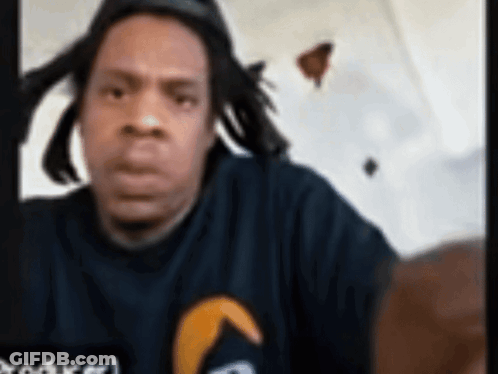 Man With Dreadlocks In Black Shirt With Yellow Arrow GIF