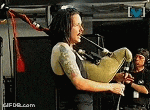 Man With Dreadlocks Playing Bagpipe On Stage GIF