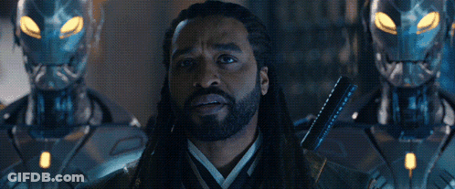 Man With Dreadlocks Standing Before Two Robots The Illuminati Above GIF