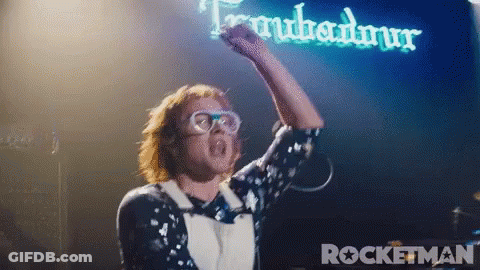 Man With Fist In Air In Front Of Rocketman Sign GIF