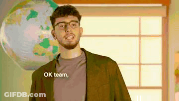 Man With Glasses And Beard Saying Ok Team In Front Of Globe GIF