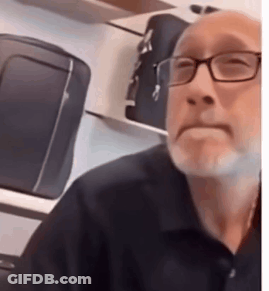 Man With Glasses And Beard Sitting At Luggage Shelf GIF