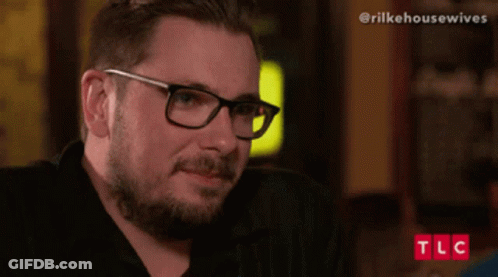 Man With Glasses And Beard Sitting In Front Of TLC Screen GIF