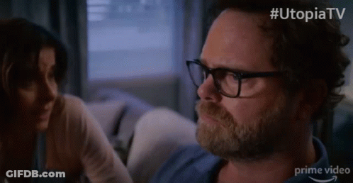 Man With Glasses And Beard Sitting On Couch With Woman Behind GIF