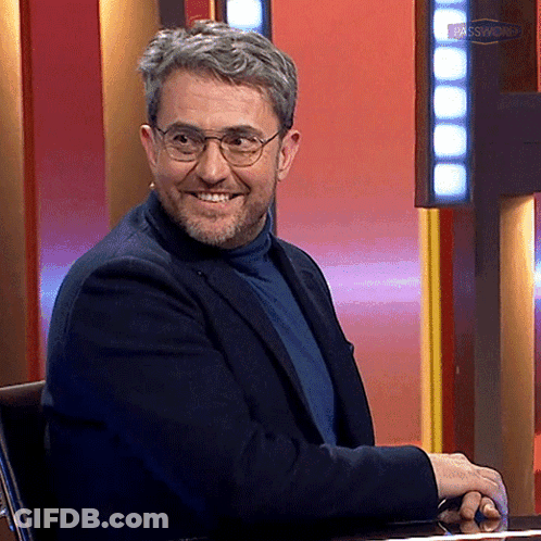 Man With Glasses And Beard Smiling In Front Of Das Samstags Sign GIF