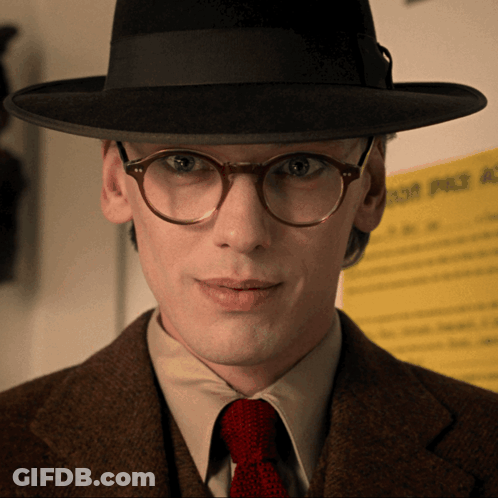 Man With Glasses And Hat In Front Of Yellow Sign Saying A GIF