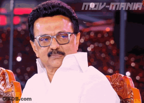 Man With Glasses And Mustache Sitting At Movi-Mania Sign GIF