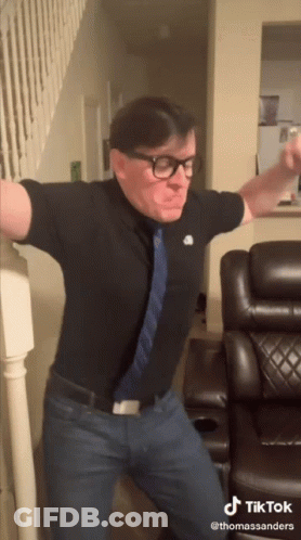 Man With Glasses And Tie Dancing In Front Of Couch And Stairs GIF