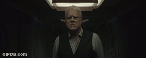 Man With Glasses And Vest Standing In Dark Room GIF