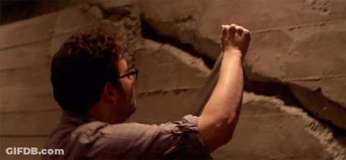Man With Glasses Holding Fist Up Against Wall GIF