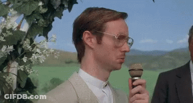 Man With Glasses Holding Microphone In Green Field GIF