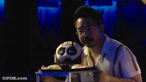 Man With Glasses Holding Puppet With Cross On Face GIF