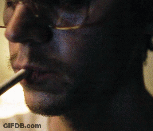 Man With Glasses Smoking Cigarette In Dark Room GIF