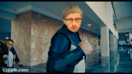 Man With Glasses Walking Down Hallway With Masked Woman Behind GIF