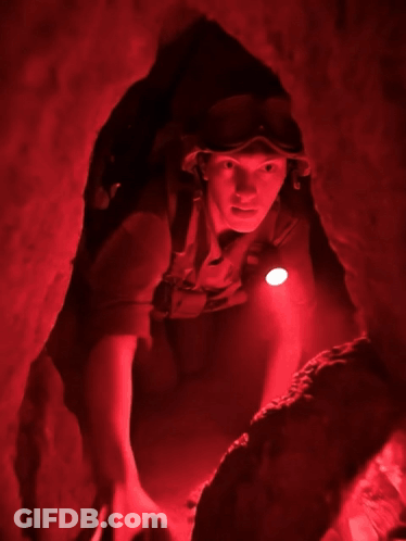 Man With Goggles And Helmet Crawling Through Cave GIF