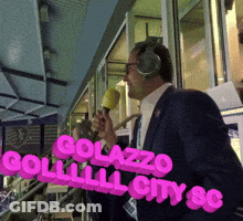 Man With Headphones Holding Microphone In Front Of Golazzo Sign GIF