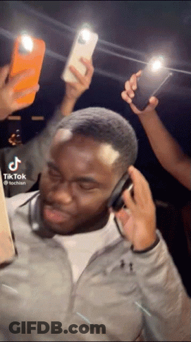 Man With Headphones Surrounded By People Holding Phones GIF