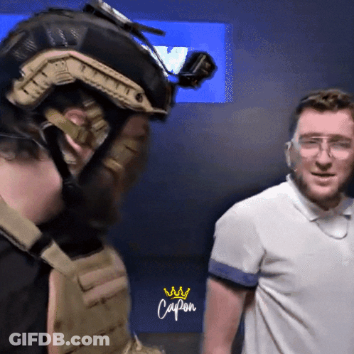 Man With Helmet And Goggles Next To Man In Capon Shirt GIF