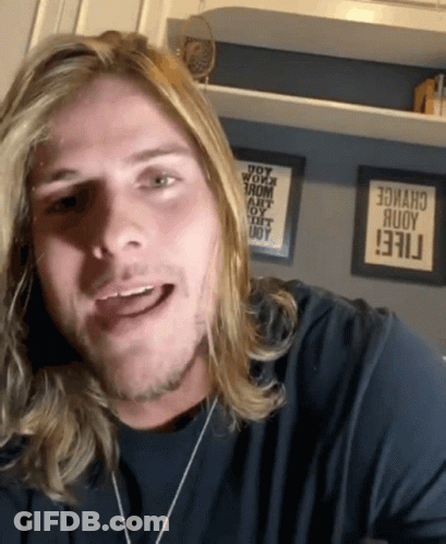 Man With Long Blonde Hair Smiling In Front Of Change Sign GIF