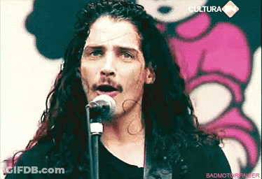 Man With Long Curly Hair And Mustache Singing Into Microphone GIF