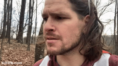 Man With Long Hair And Beard Standing In Woods GIF