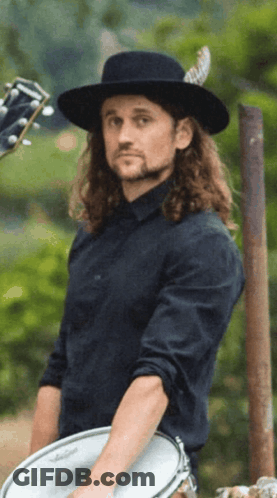 Man With Long Hair And Black Hat Holding Drum GIF