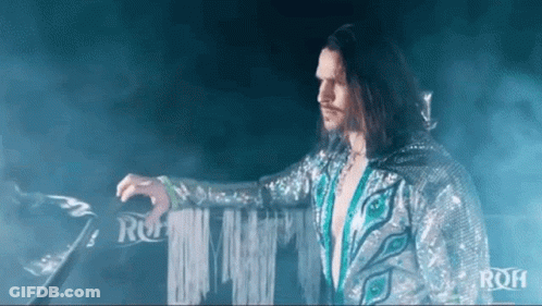 Man With Long Hair And Peacock Feather Costume Standing In Ring GIF