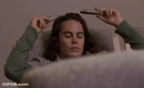Man With Long Hair Laying In Chair Holding Pipe To Head GIF